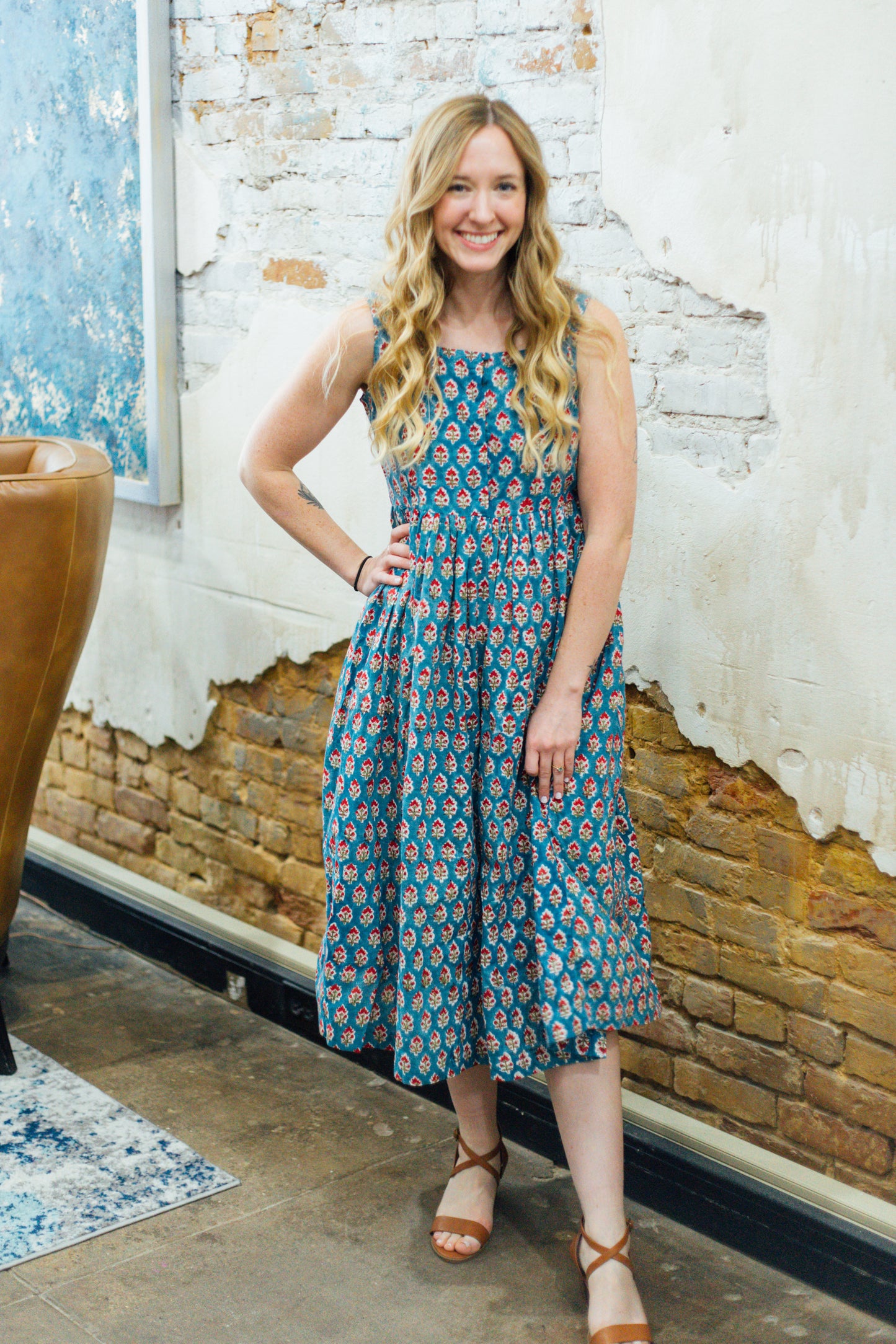 A woman standing indoors wearing a blue and red floral dress with three-quarter sleeves and a square-neckline.