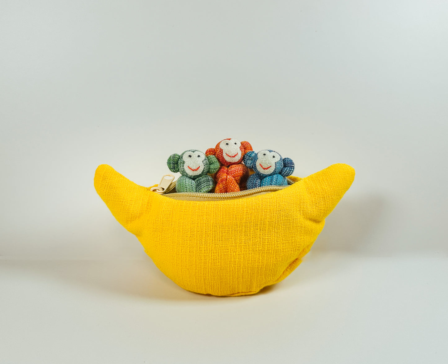 A yellow zippered fabric banana toy with three colorful mini stuffed animals inside.