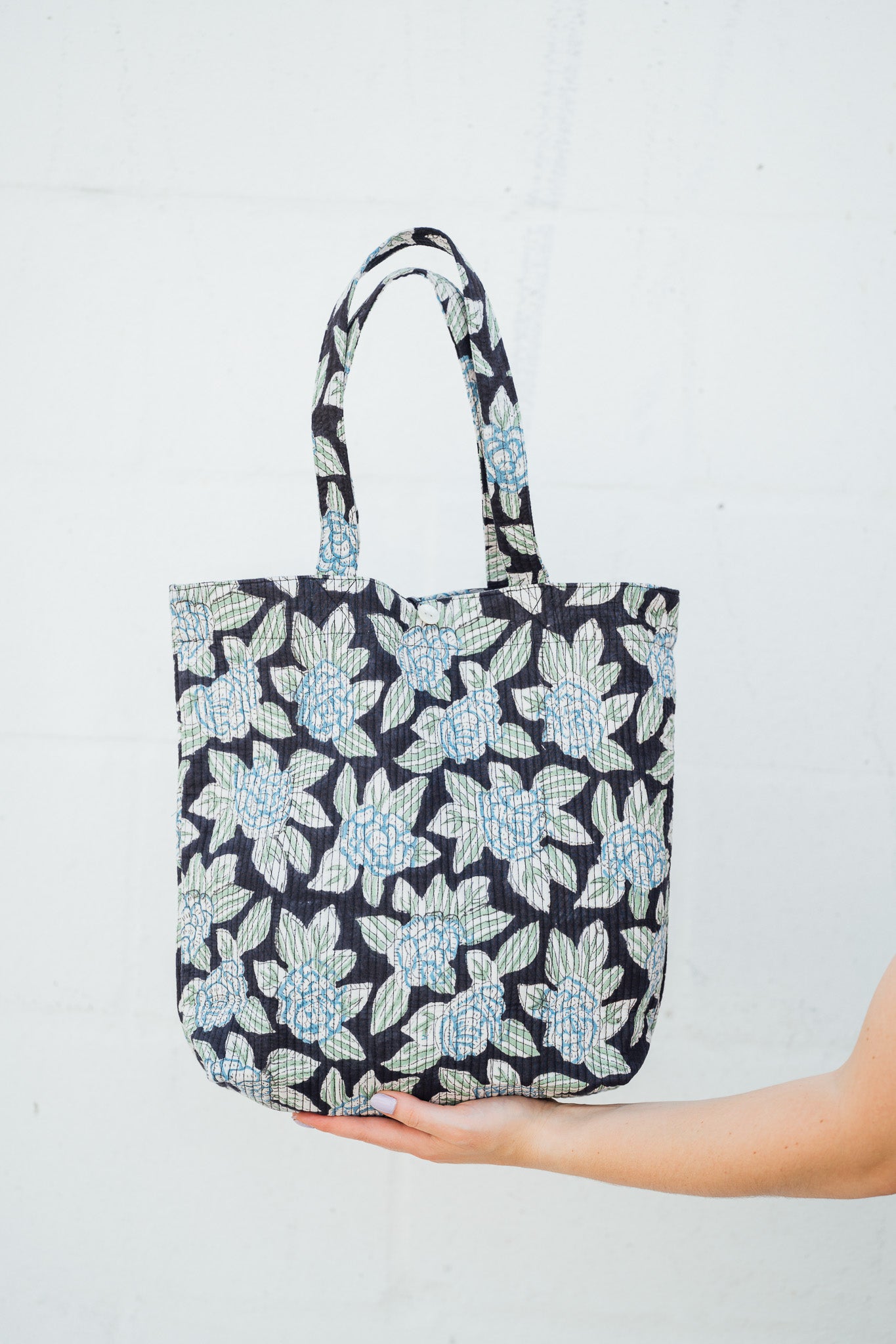 Black Floral Boho Quilted Indian Tote bag held by a hand on a light gray background