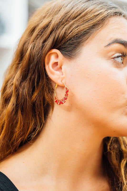 Close-up of a person wearing a gold hoop earring with red accents.