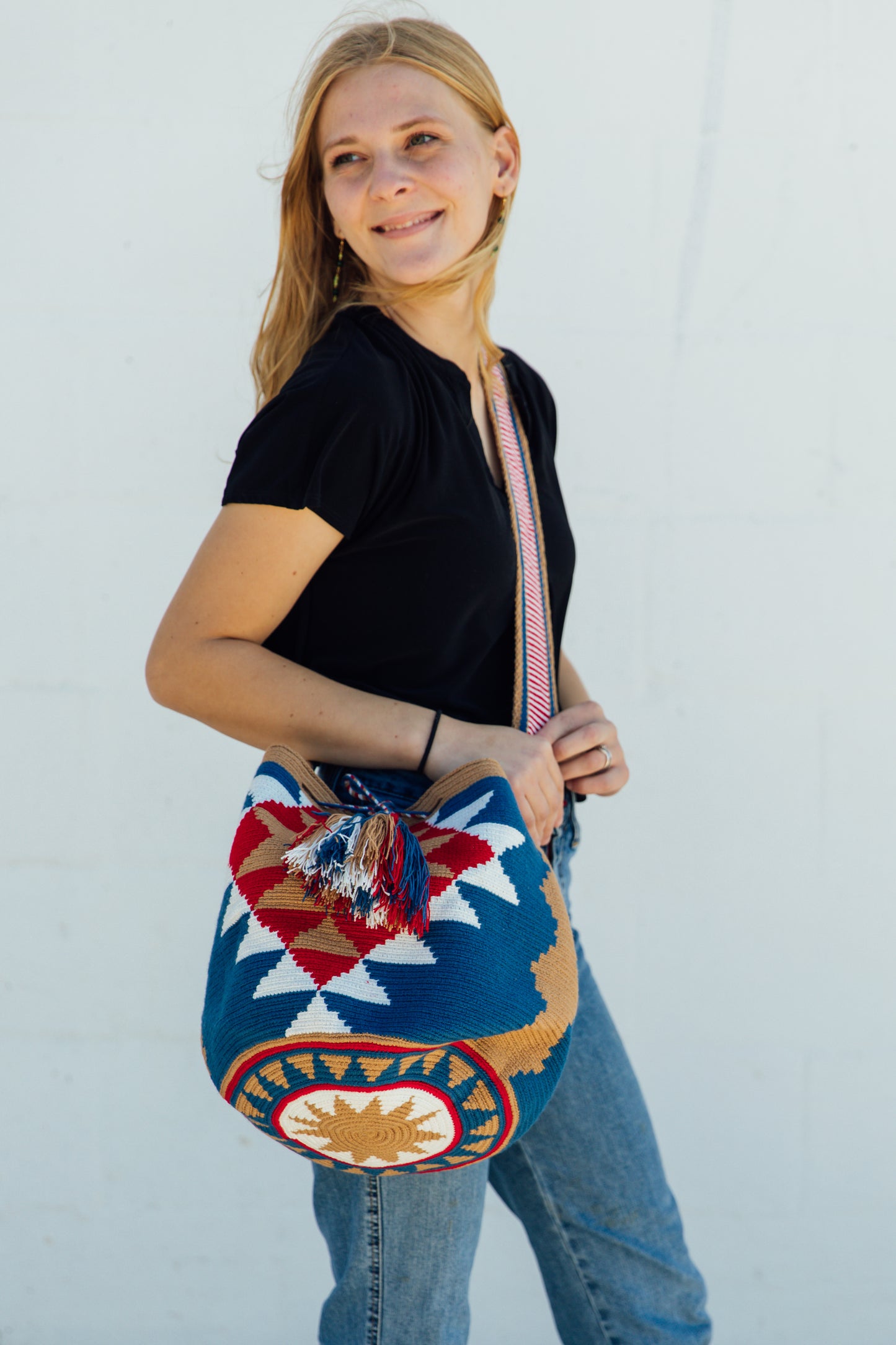 a model wearing a tan, red, and blue wayuu bag