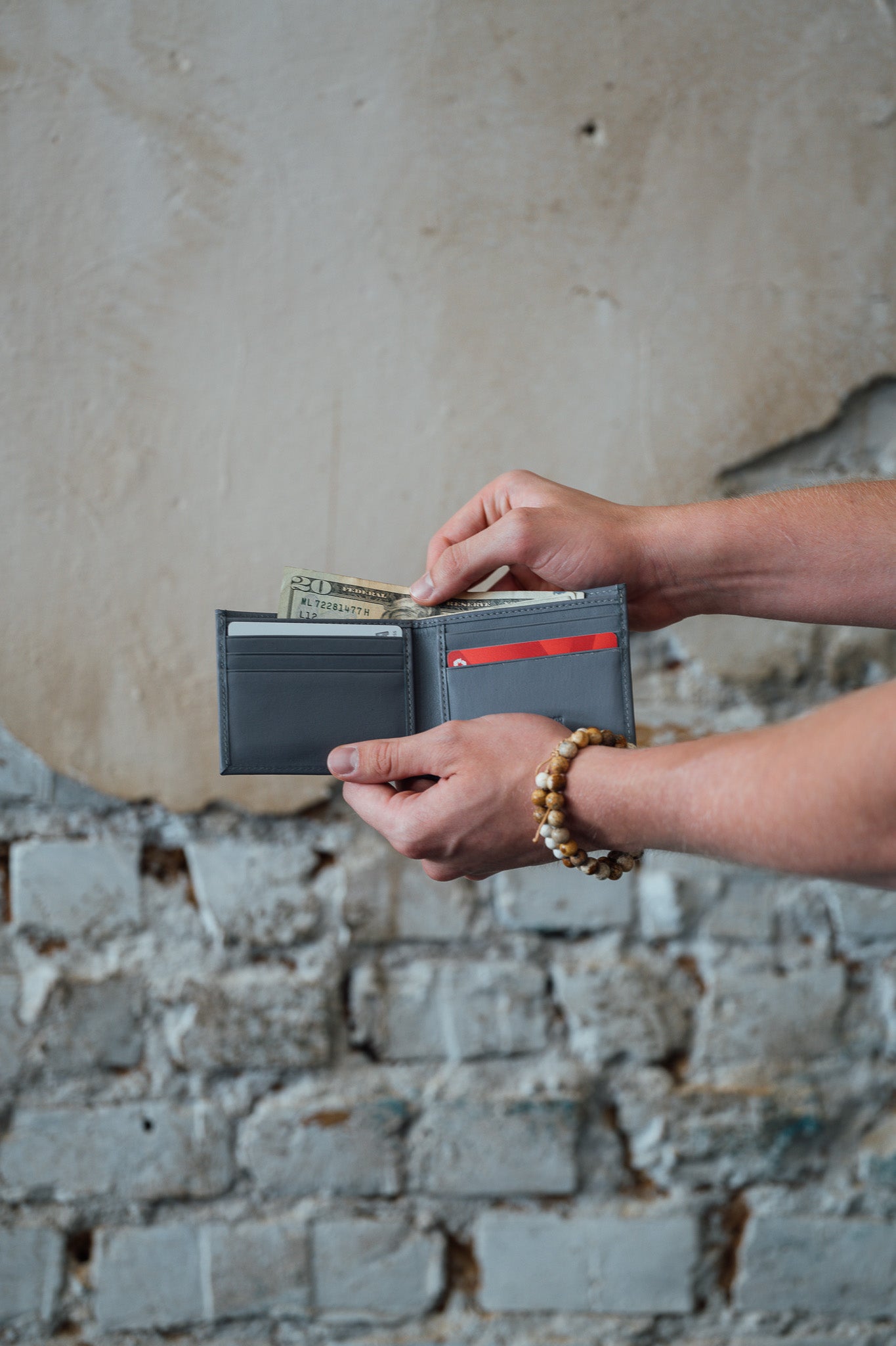 Person holding a Slim Bifold Leather Wallet with money against a stone wall background