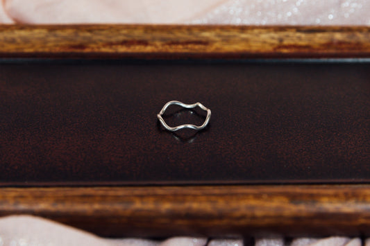 A silver ring with a sleek design placed on a wooden surface, with a close-up view primarily showcasing the ring's design.