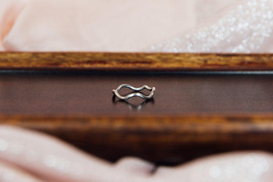 A silver ring with a sleek design placed on a wooden surface, with a close-up view primarily showcasing the ring's design.