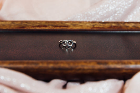 A silver ring with a sleek design, featuring a infinity symbol, displayed on a wooden surface.