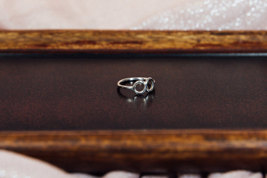 A side view of a silver ring with a sleek design, featuring a infinity symbol, displayed on a wooden surface.