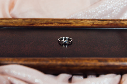 A side view of a silver ring with a sleek design displayed on a wooden surface.