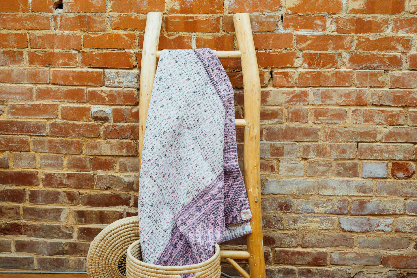 A purple baby blanket made from quilted kantha material hanging on a blanket ladder.