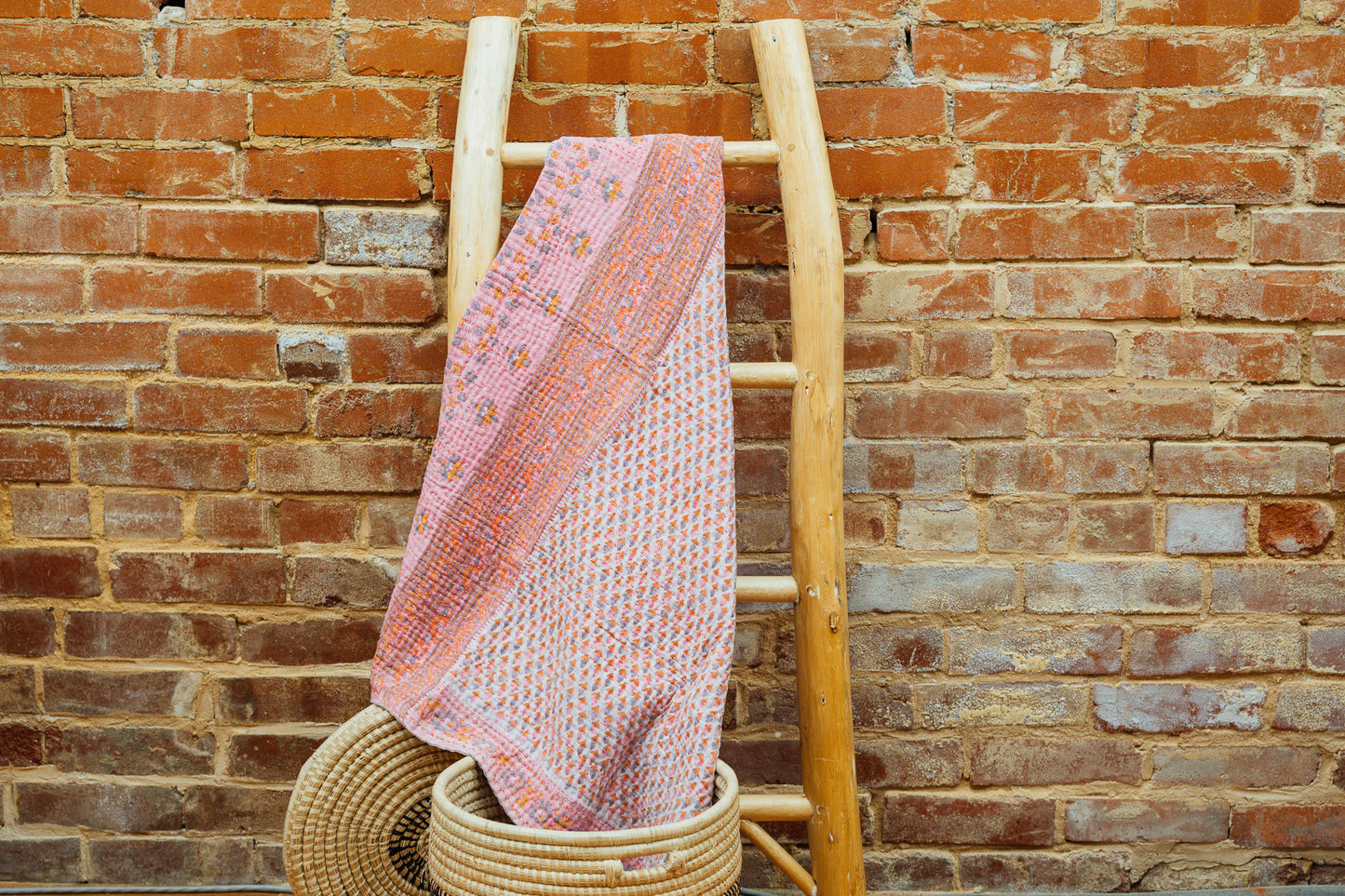A pink baby blanket made from quilted kantha material hanging on a blanket ladder.
