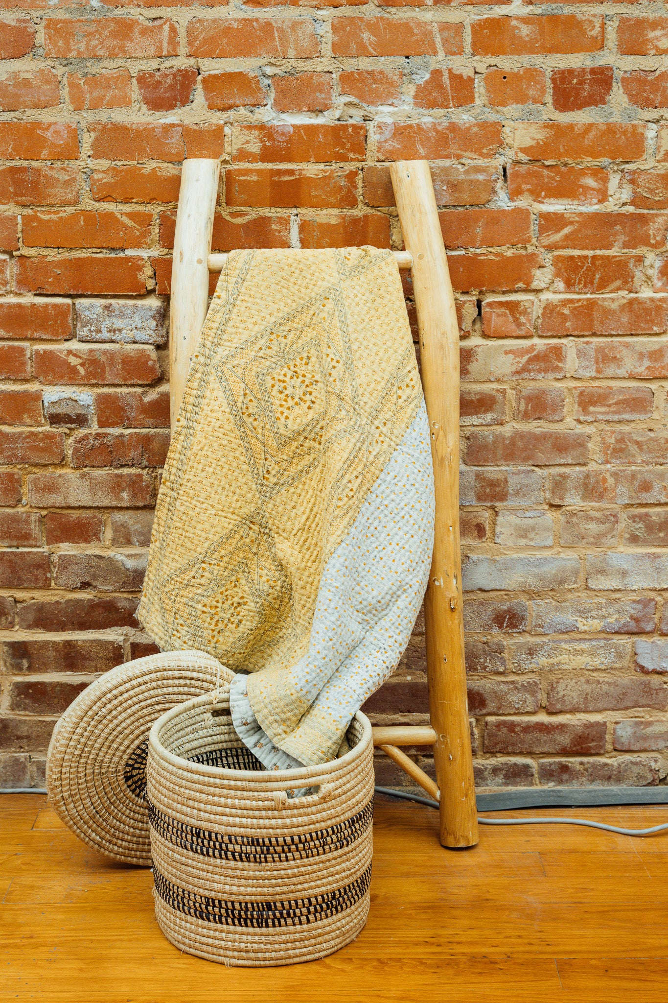 A yellow baby blanket made from quilted kantha material hanging on a blanket ladder.