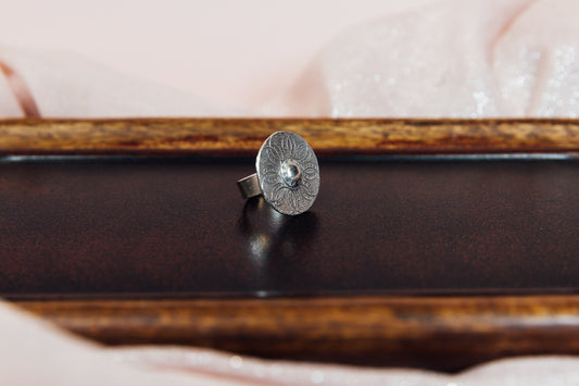A silver ring with an intricate circular pattern, displayed on a wooden surface.