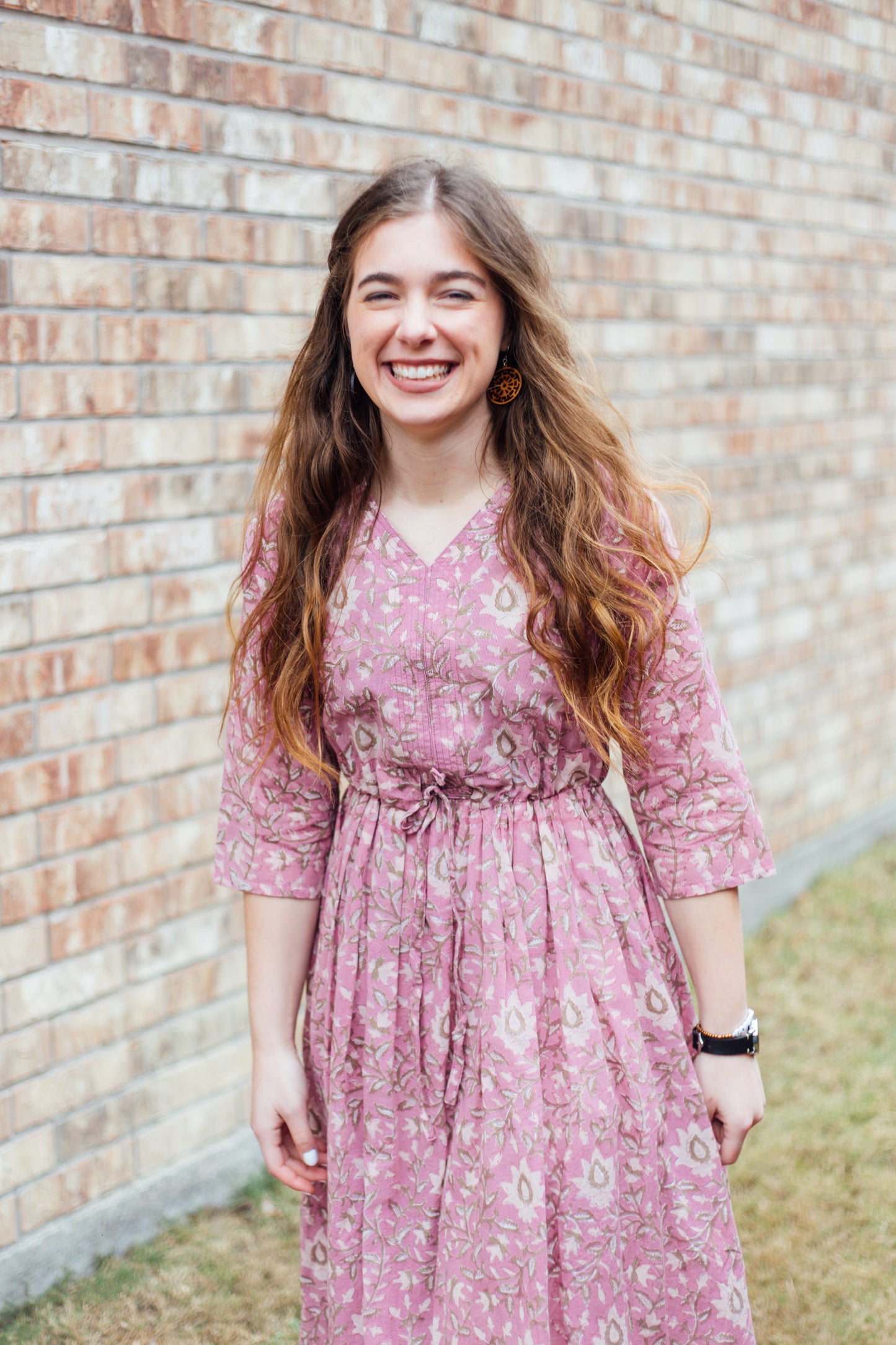 A women wearing a pink floral dress with 3/4 length sleeves and a v-neckline