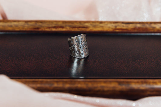 A silver ring with an intricate floral pattern, displayed on a wooden surface.