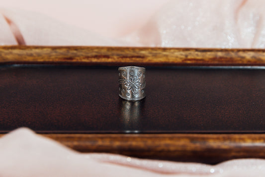 A silver statement ring with a floral design displayed on a wooden surface