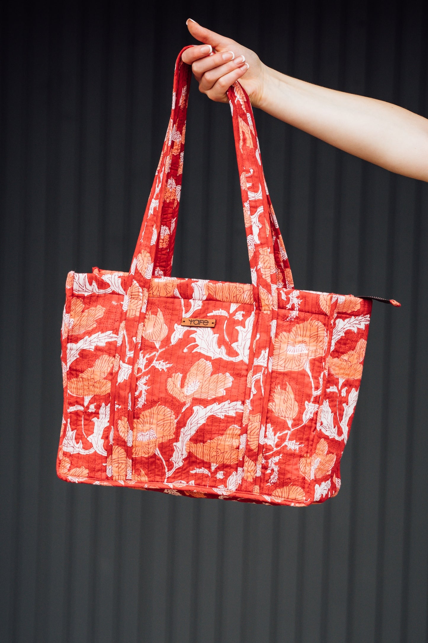 Red floral patterned tote bag held by a hand against a black background