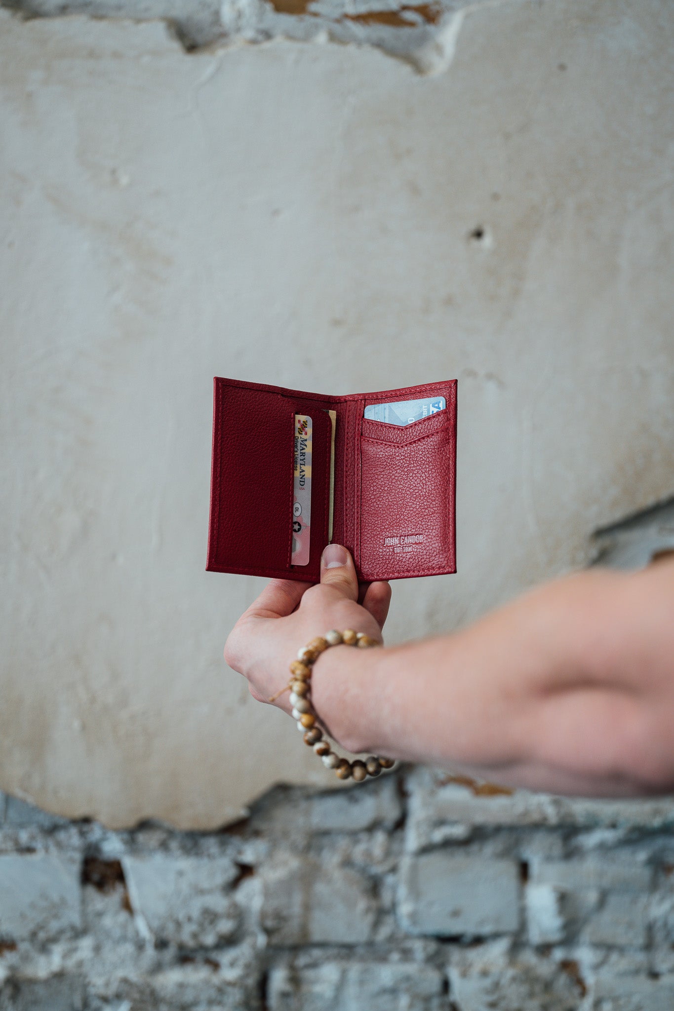 Red wallet held by a hand against a textured wall background