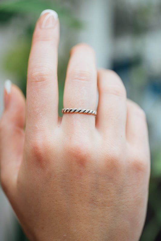 Close-up of a hand wearing a braided silver ring with a blurred natural background