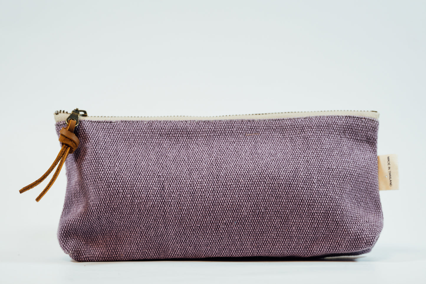 A purple fabric pencil case with a metal zipper and a leather tassel, against a white background.