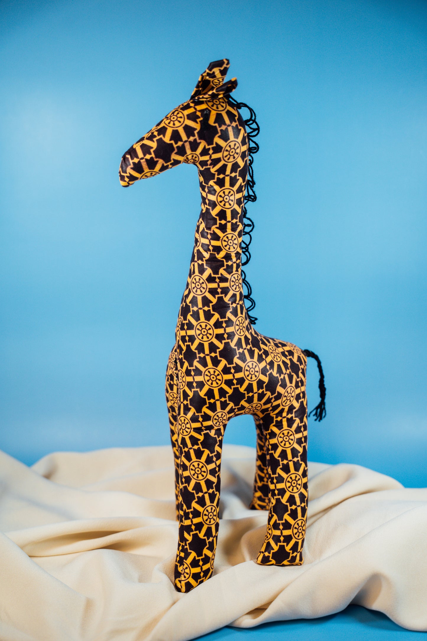 A handcrafted giraffe made from vibrant African fabric, displayed against a blue background.
