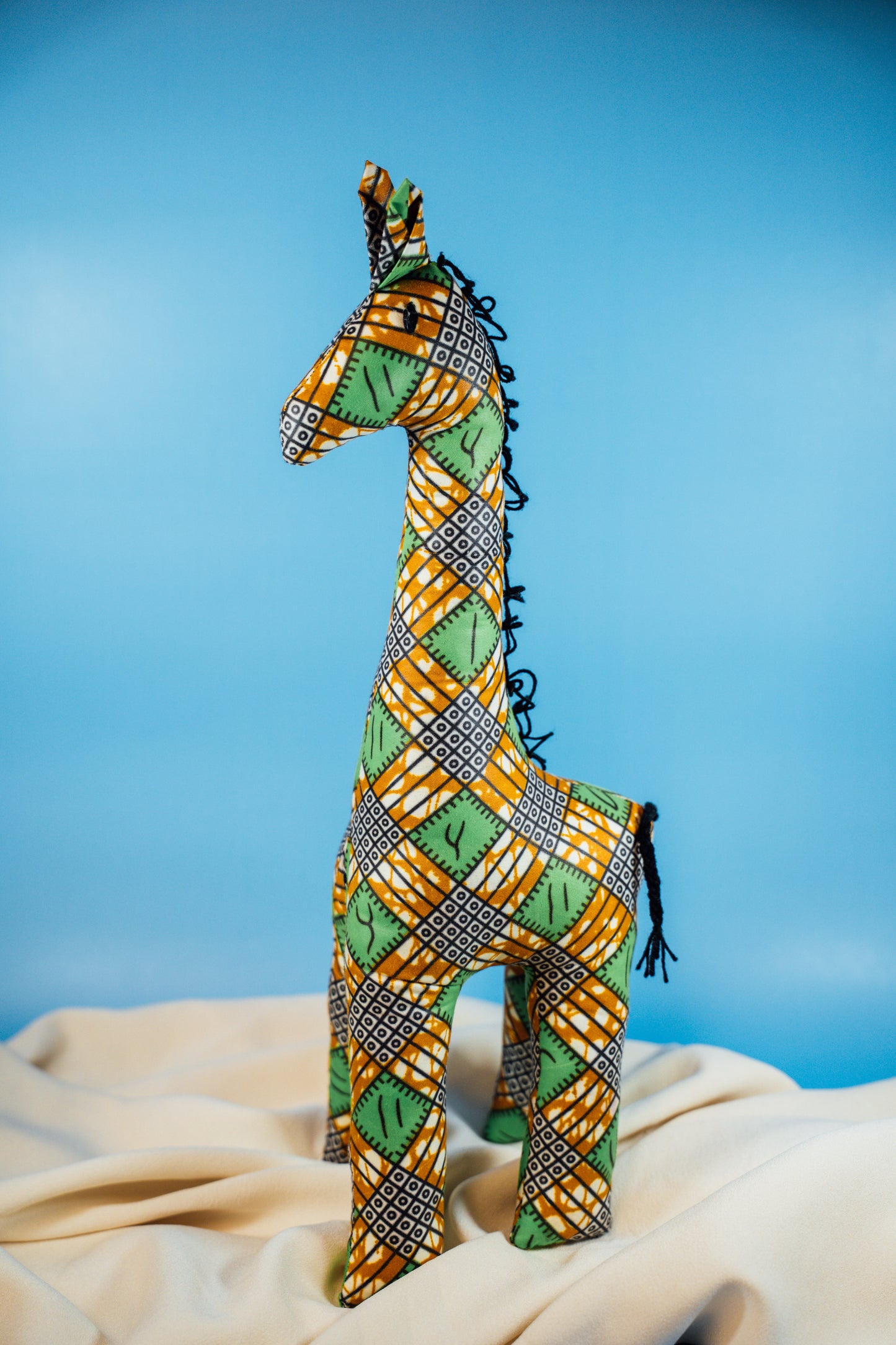 A handcrafted giraffe made from vibrant African fabric, displayed against a blue background.
