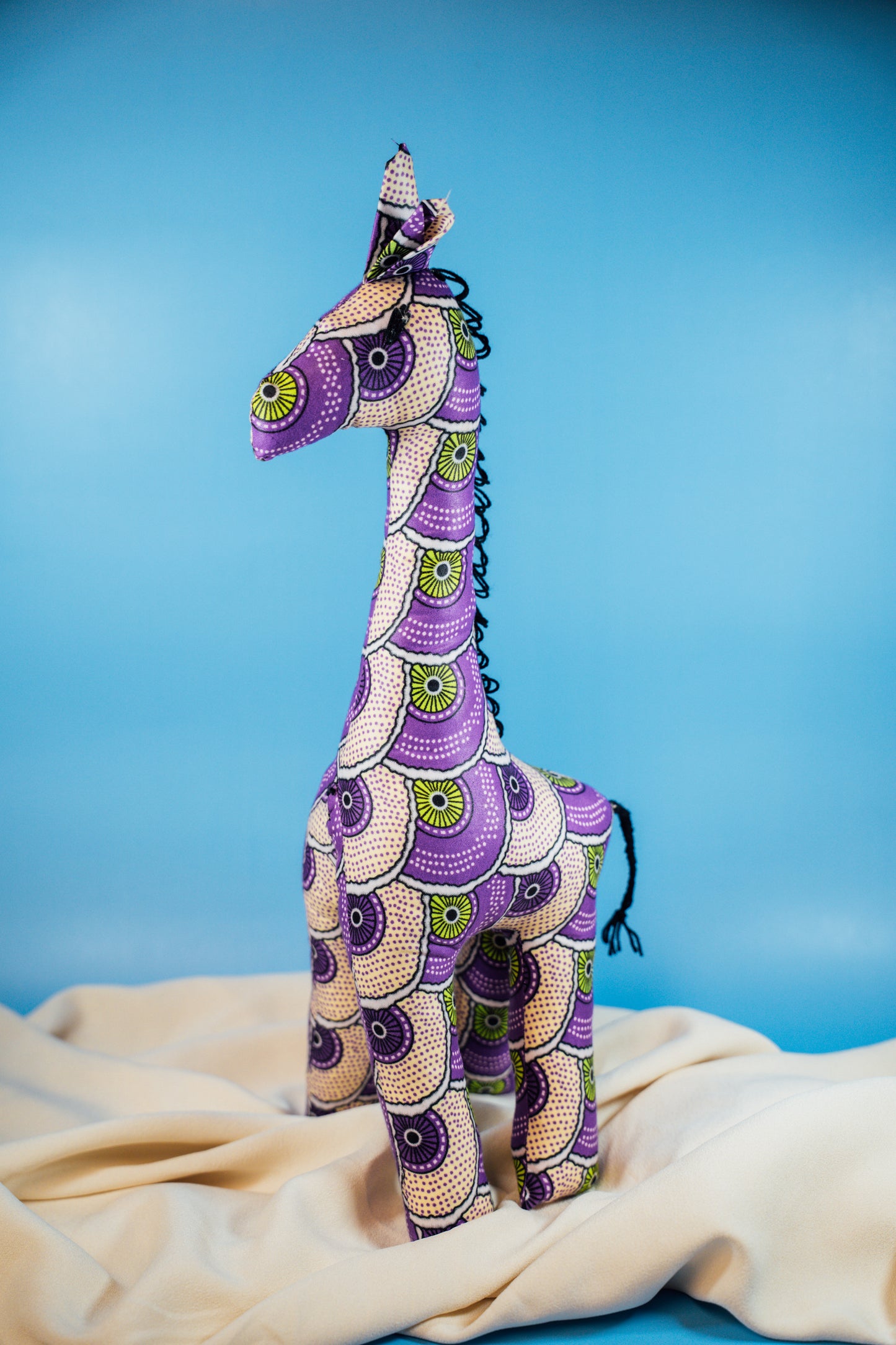 A handcrafted giraffe made from vibrant African fabric, displayed against a blue background.