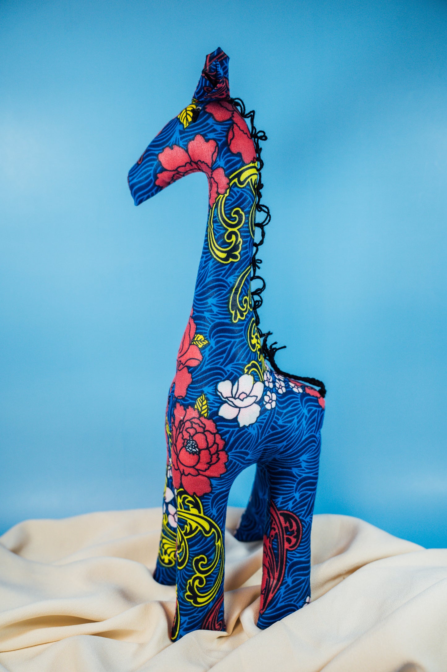 A handcrafted giraffe made from vibrant African fabric, displayed against a blue background.