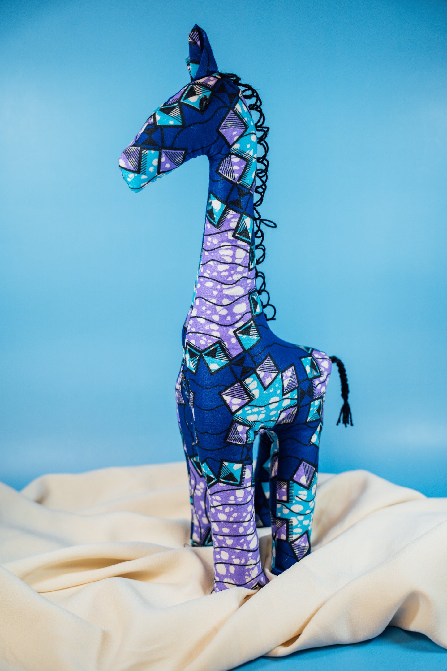 A handcrafted giraffe made from vibrant African fabric, displayed against a blue background.