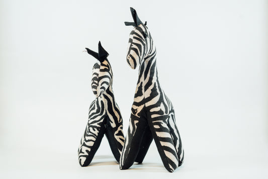 Two handcrafted cloth zebras with black-and-white stripes, made in Uganda, displayed against a white background.