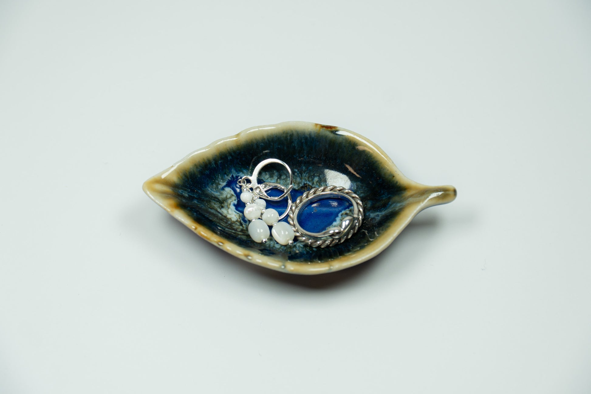 Ceramic leaf-shaped dish with jewelry on a light gray background