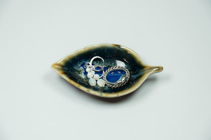 Ceramic leaf-shaped dish with jewelry on a light gray background
