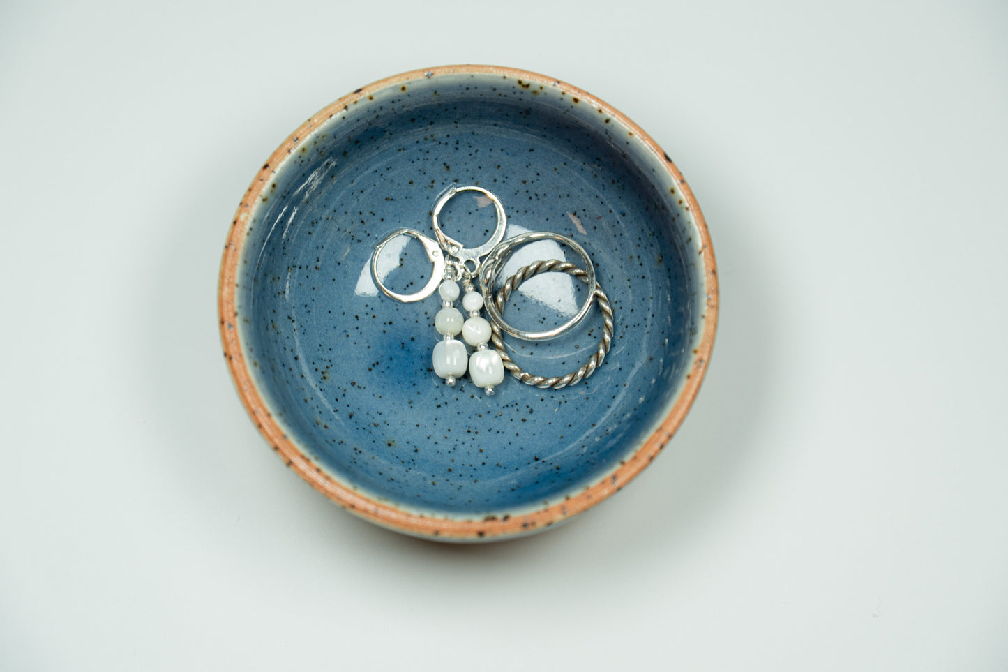 Blue ceramic dish with jewelry on a light gray background