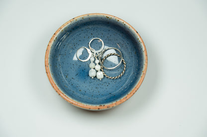 Blue ceramic dish with jewelry on a light gray background