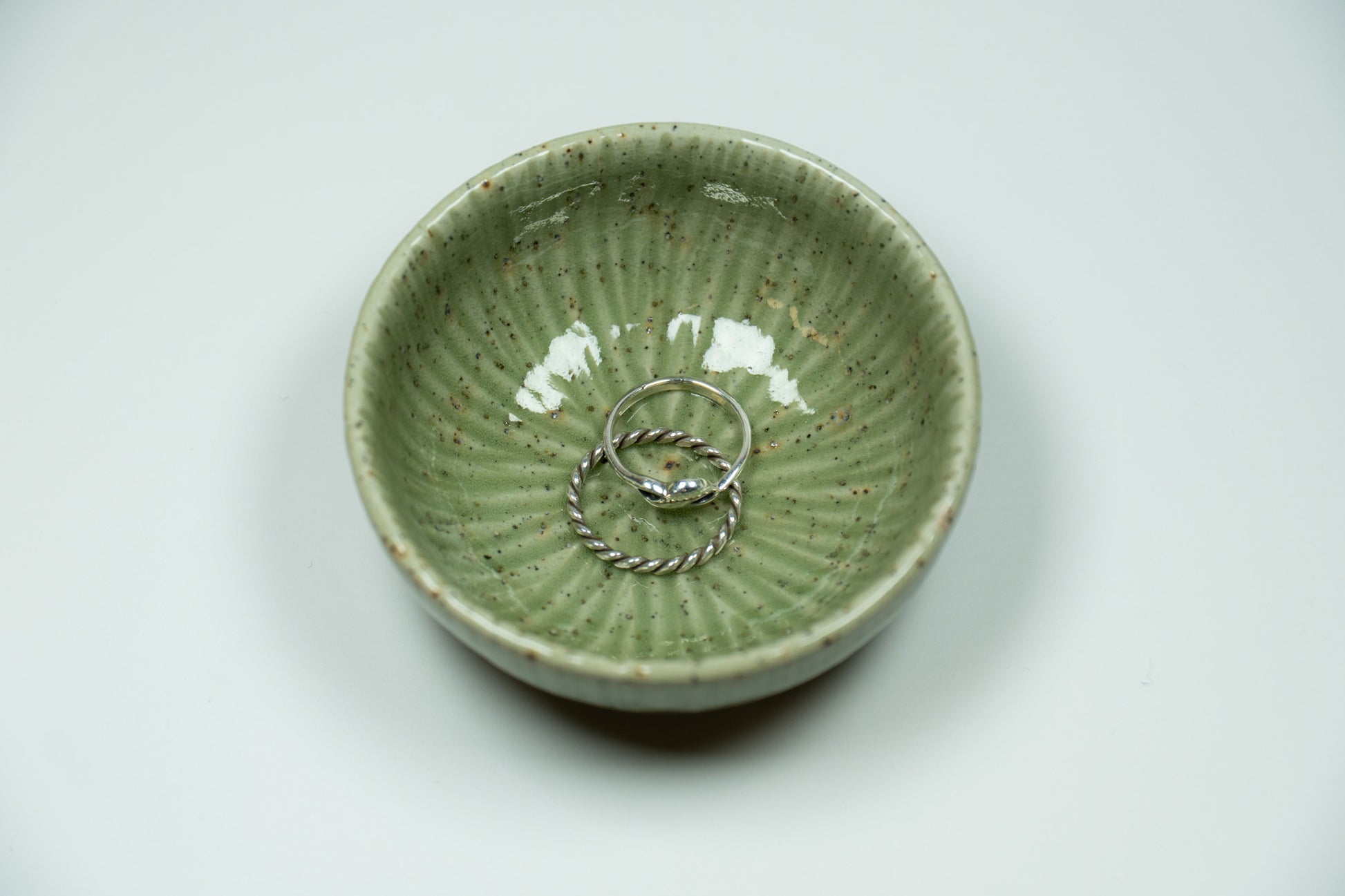 Green ceramic bowl with two silver rings on a light gray background