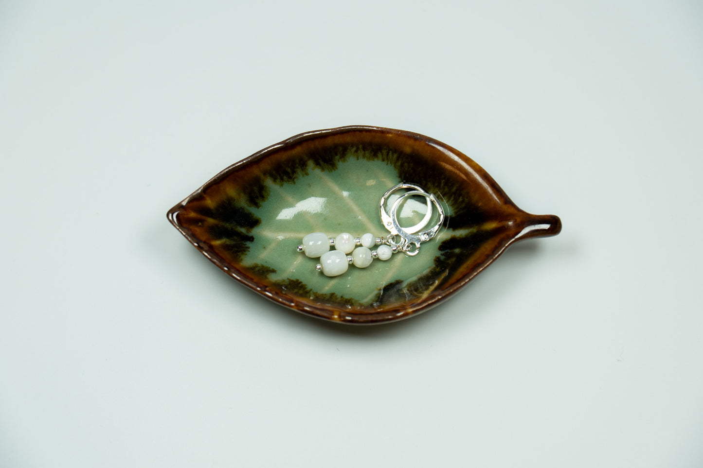Ceramic leaf-shaped dish with jewelry on a light gray background