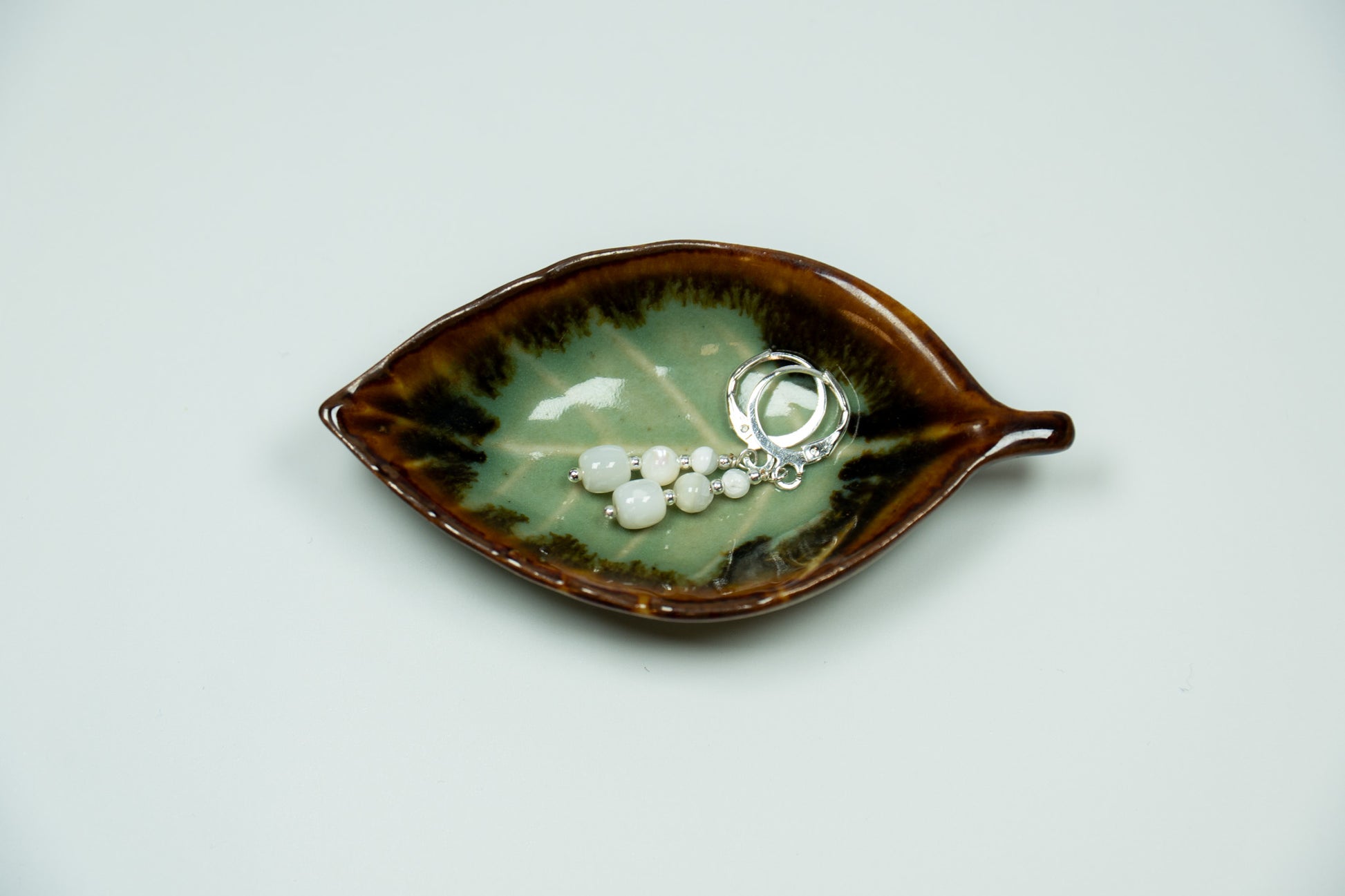 Ceramic leaf-shaped dish with jewelry on a light gray background
