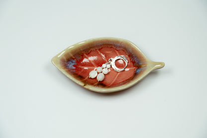 Ceramic leaf-shaped dish and a silver earrings on a white background