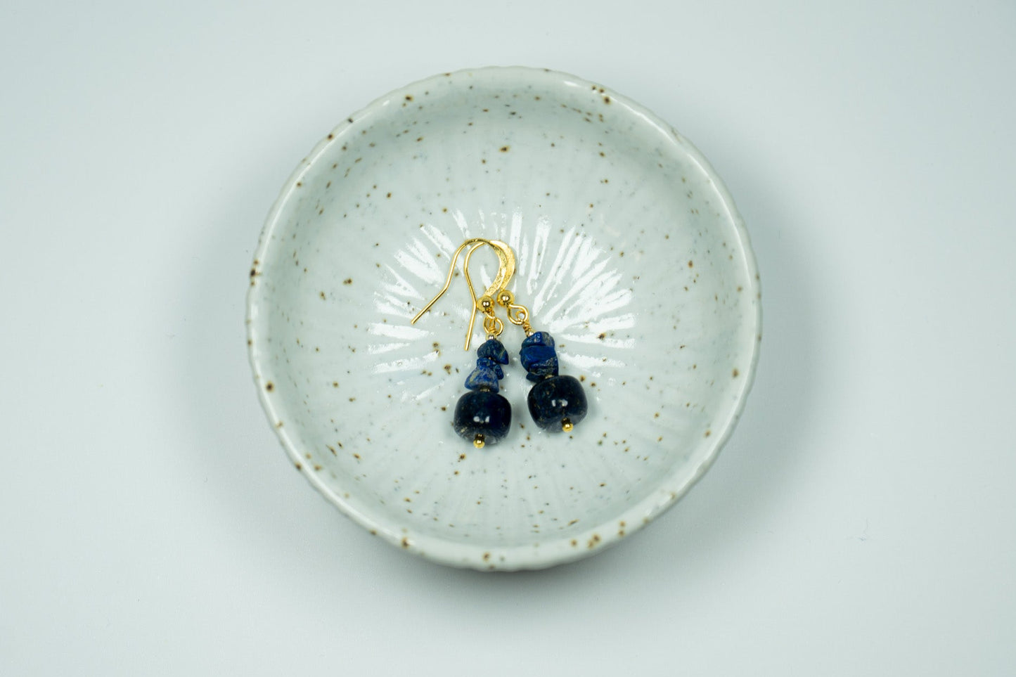 Pair of blue earrings in a white ceramic trinket bowl with a white background