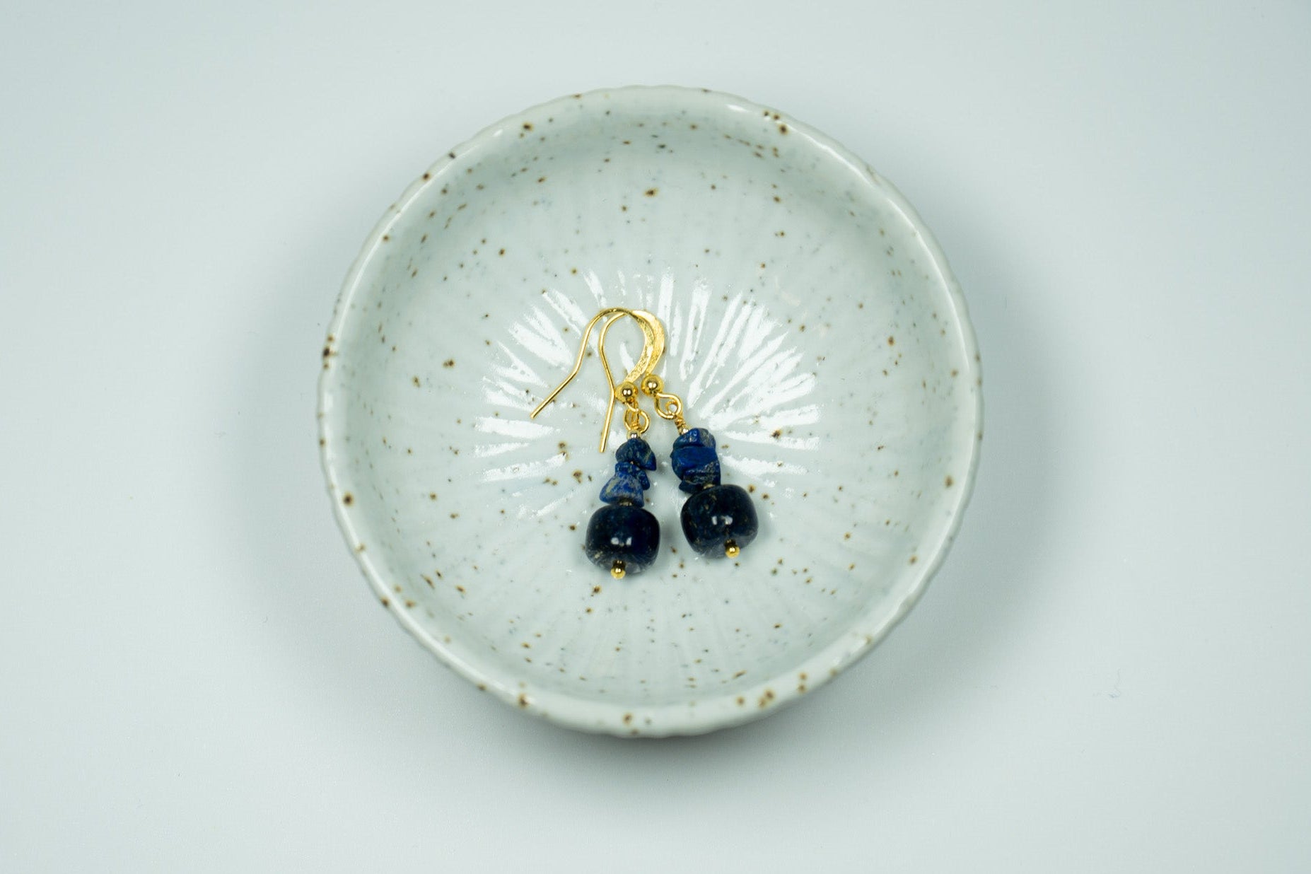 Pair of blue earrings in a white ceramic trinket bowl with a white background