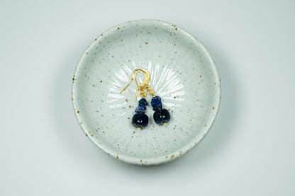 Pair of blue earrings in a white ceramic trinket bowl with a white background