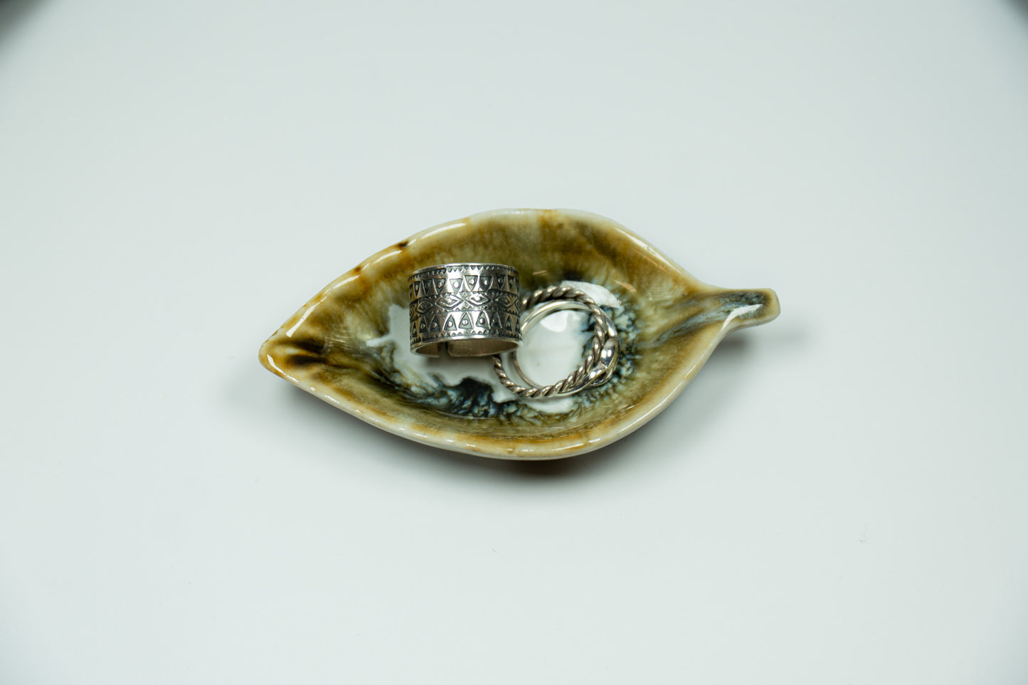 Two silver rings on a leaf-shaped ceramic dish with a white background