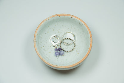 Two silver rings with purple stones in a ceramic dish on a light gray background