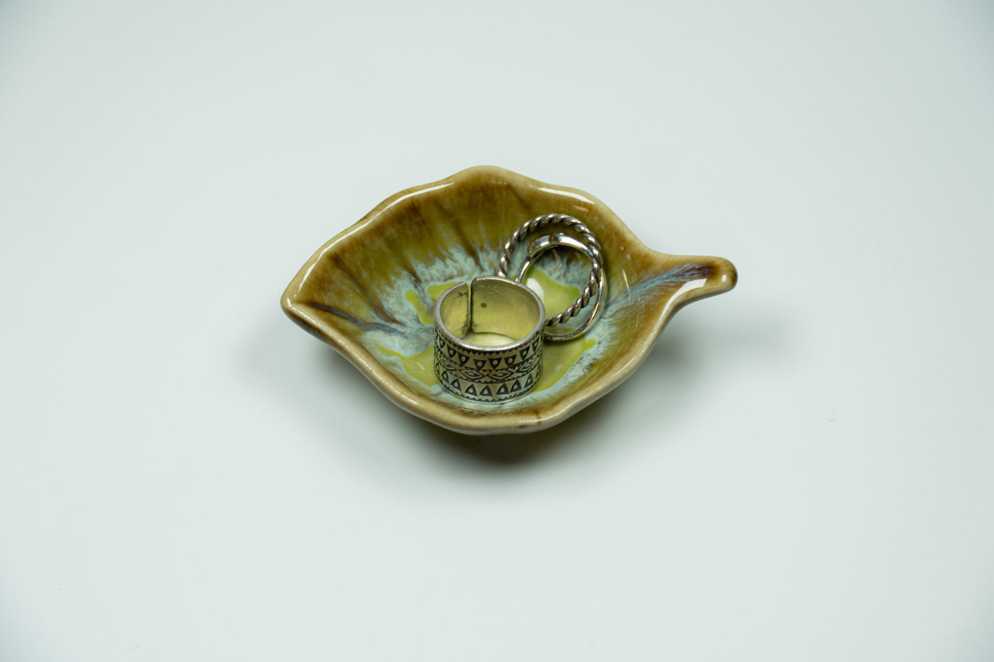 Ceramic leaf-shaped dish with silver rings on a white background