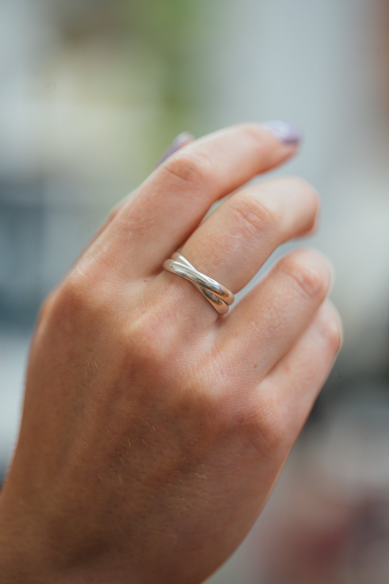 Hand wearing a silver ring with a blurred background