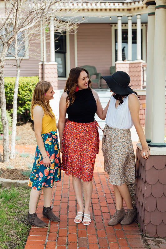 Three women standing on a brick pathway, wearing midi wrap skirts with floral and solid patterns.