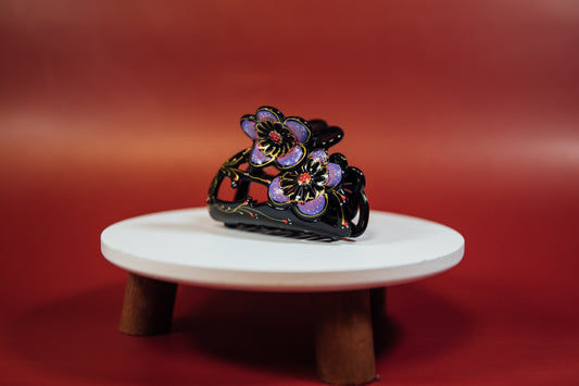 A hand painted Medium Flower claw clip with a unique design, displayed on a white stand against a red background.