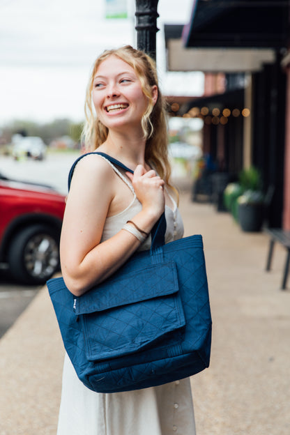 A woman standing on the sidewalk holding a navy tote bag with quilted design.
