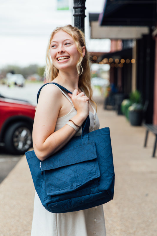 A woman standing on the sidewalk holding a navy tote bag with quilted design.