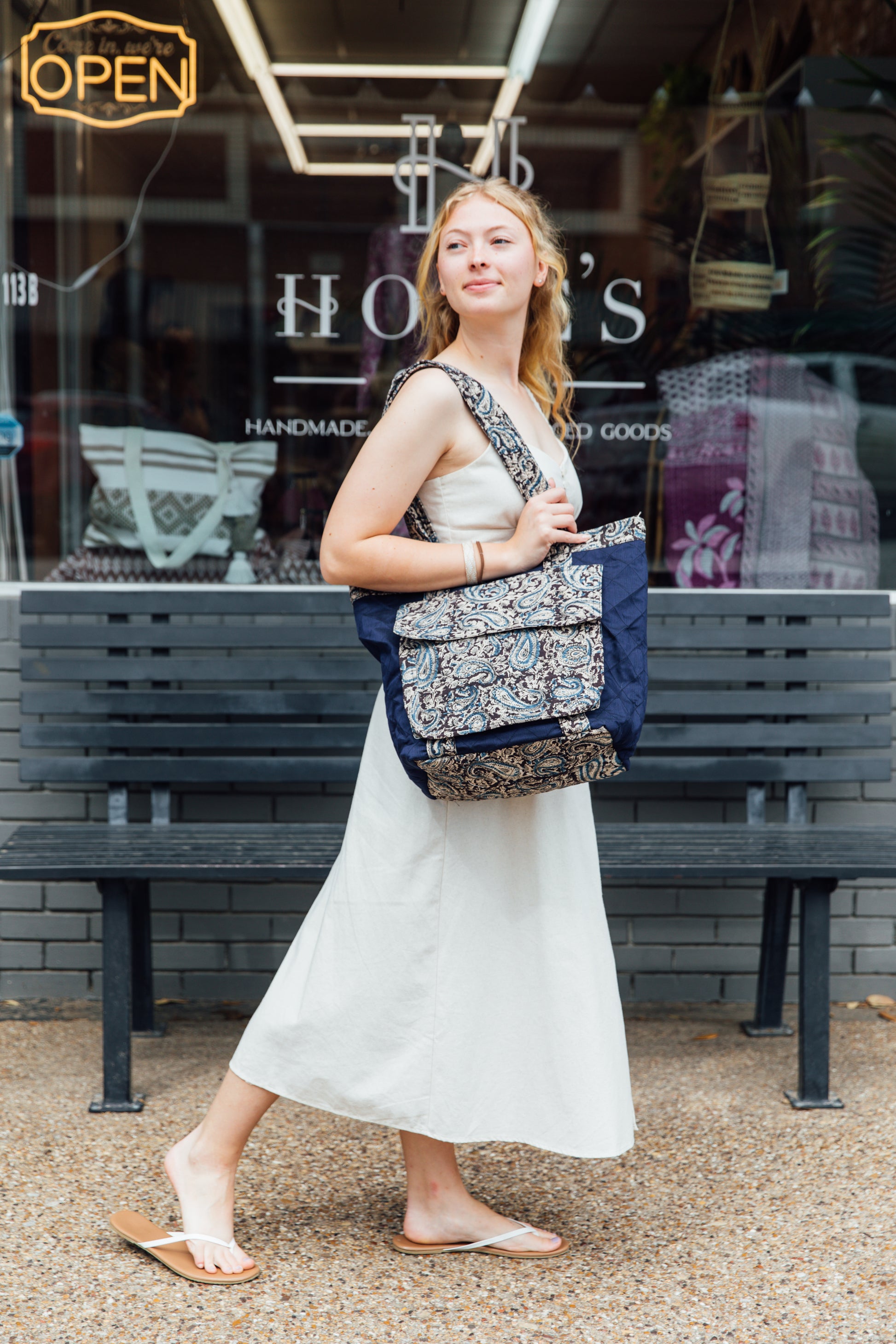 A woman standing on the sidewalk holding a blue tote bag with a black and blue block-printed quilted design.