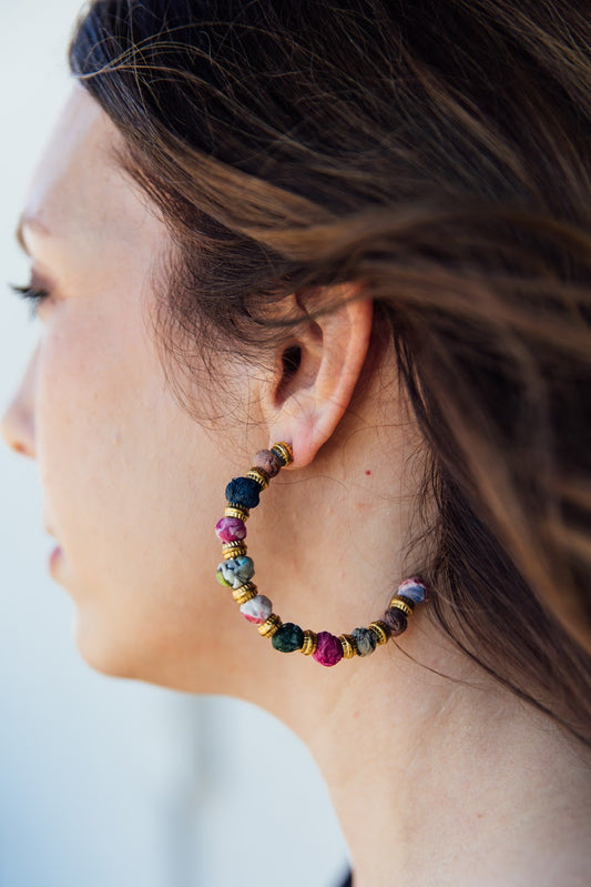 A side profile of a person wearing a large hoop earring with multicolored fabric beads.