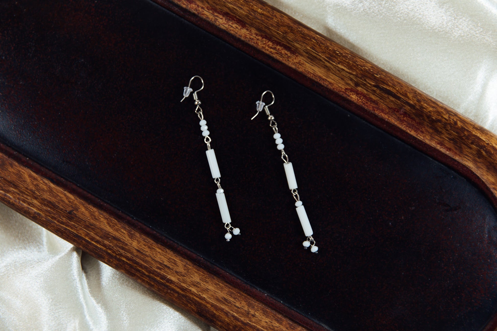 White beaded dangle earrings displayed on a wooden surface